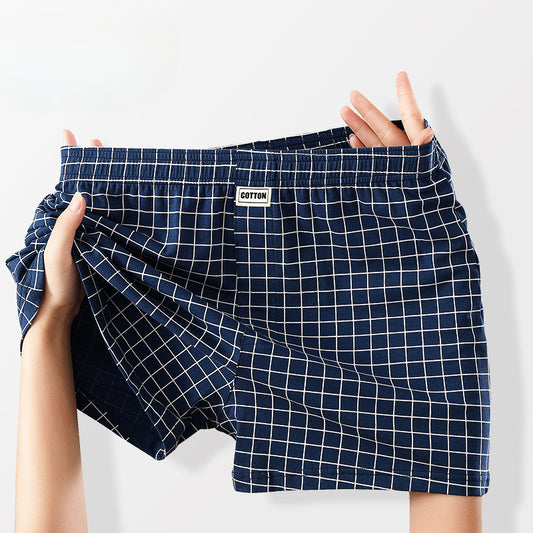 A pair of men's boxer briefs with a navy blue and white grid pattern, held up by a person's hands against a light gray background.