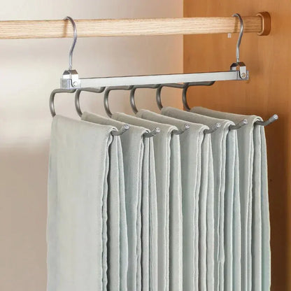Multi-tier metal pants hanger with six hooks holding folded gray pants in wooden closet