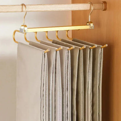 Golden multi-tier pant hanger with beige trousers hanging in a wooden closet
